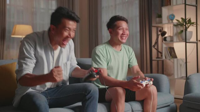 Asian Friends With Joystick Playing Video Games And Celebrating Victory At Home
