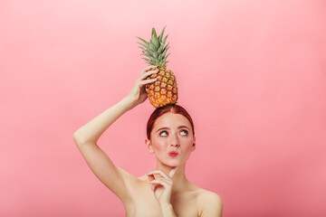 Pensive nude woman holding pineapple. Ginger caucasian girl with exotic fruit and looking away.