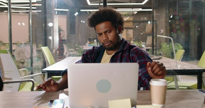 Pensive African graphic designer focusing to come up with interesting ideas. Freelancer working on laptop smiling when overcoming new challenge 4k footage