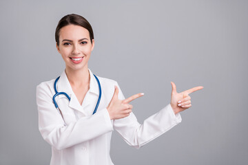 Photo of adorable cute young doc woman dressed white coat smiling pointing fingers empty space...