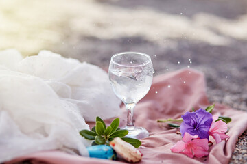 Gin tonic cocktail in wine glass on beach with flowers and macaroons. Delicate silk materials and bokeh background. Refreshing summer concept