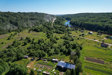 aerial view river flowing village on the river bank in the middle of the forest dust on a dirt road from a passing car