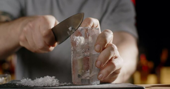 Bartender makes crushed ice from large ice cube by sharp knife, making the cocktail on the bar counter, refreshing cold drinks, 4k Prores HQ 120fps