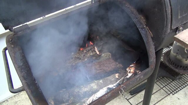 A barbeque wood smoker with a bunch of logs on fire and smoke coming from it