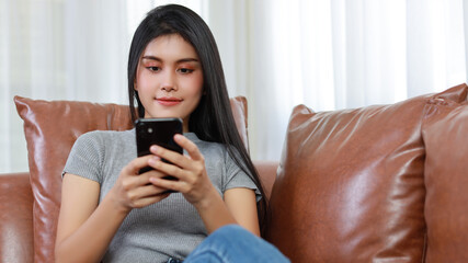 Young smart and active asian female sitting on sofa in living room, using smartphone with wireless...