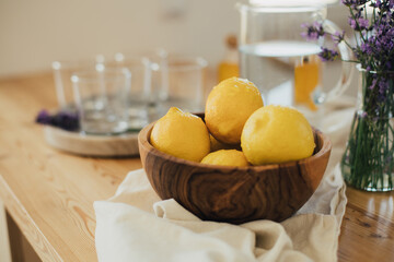Wooden bowl with fresh lemons, emty glasses on a tray standing on a kitchen table.