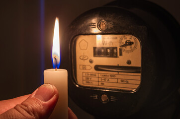 Power outage or blackout concept image. Person's hand with candle shining light in the dark near...