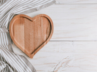 Heart on wooden background.
An empty heart-shaped plate with a kitchen napkin lie on the left on a wooden table with space for text on the right, top view close-up.