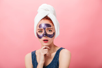 Front view of adorable girl doing spa treatment. Studio shot of wonderful caucasian lady with face mask isolated on pink background.