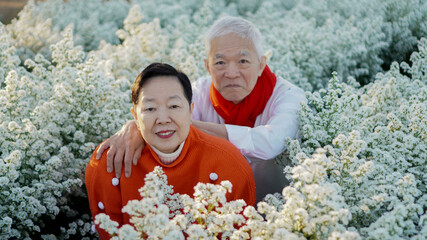 Asian senior eldery couple hugging sweater celecrate Christmas and New Year holiday morning in beautiful flowers garden