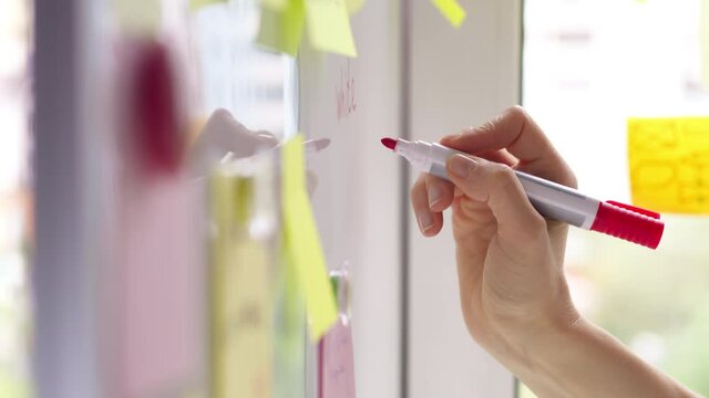 Business woman's hand writes a note with a marker on a white board using on the paper stickers post. Brainstorming, teamwork. 