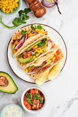 Mexican tacos with grilled chicken, avocado, corn kernels, tomato, onion, cilantro and salsa at white stone table. Traditional Mexican and Latin american street food. Top view.