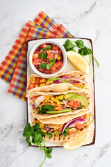 Mexican tacos with grilled chicken, avocado, corn kernels, tomato, onion, cilantro and salsa at white stone table. Traditional Mexican and Latin american street food. Top view.