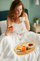 Happy woman enjoying breakfast in bed