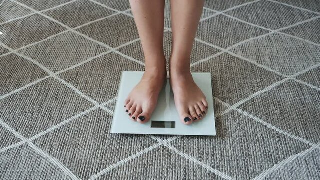 Weighing on scales, woman legs standing on scales standing on floor at home