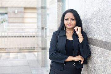 An Indian woman standing with her arms crossed in an urban corporate setting.