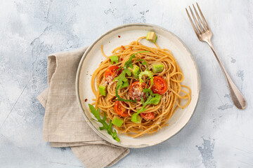 Spaghetti pasta with pesto, avocado and tomatoes in rustic white plate. Raw vegan food concept. Top view.