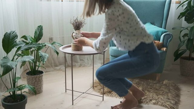 Woman decorating home interior with vase lavender, ginger cat sleeping on armchair at home
