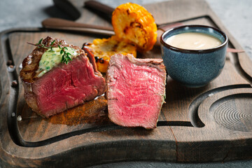 A large grilled filet Mignon steak with butter and thyme is served chopped on a wooden board. A...
