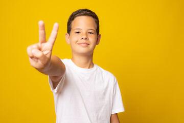 A happy shouting boy showing a victory sign isolated over yellow background