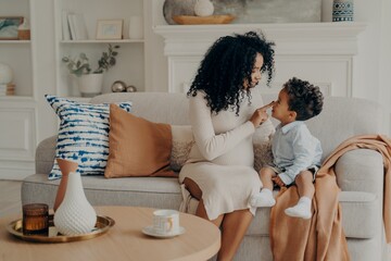 Portrait of beautiful family pregnant mother and son afro ethnic race sitting on sofa