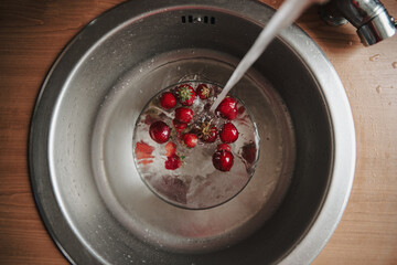 Washing up ripe strawberries in glass bowl. Rinsing red summer berries full of vitamins.