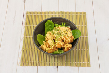 Ebi prawn tempura with spinach, oregano and parsley leaves, curry sauce and bamboo trivet on a white table.