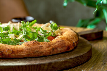 Vegetarian wood-fired pizza with arugula, vegetables and parmesan on wood board. Selective focus