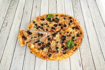 Very thin crust pizza slices with bacon, mozzarella cheese, sliced black olives, basil leaves and...