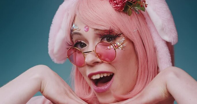 Close up of pink cute candy anime girl with rabbit ears and pink sunglasses make emotional grimaces and flirting on isolated on blue background. Beautiful asian cosplay anime teen girl concept