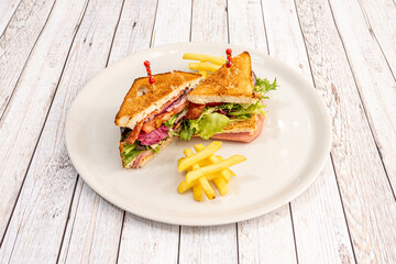 Typical club sandwich with layers of lettuce, sliced tomato, bacon, red onion, ham and grilled sliced bread