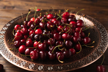 a lot of ripe cherries are lying on a copper tray with a pattern.