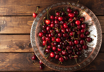 a lot of ripe cherries are lying on a copper tray with a pattern.