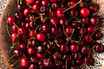 a lot of ripe cherries are lying on a copper tray with a pattern.