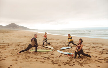 Group of people stretching at the beach, before starting a surf session - 443857837