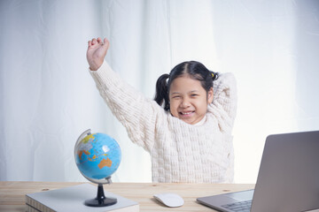 Asian kid girl writing follows teacher for learning an online lesson by video call the Internet...