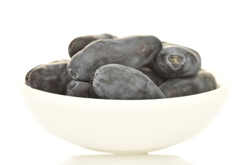 Several dark blue organic ripe honeysuckle berries in a white bowl, close-up, isolated on white.