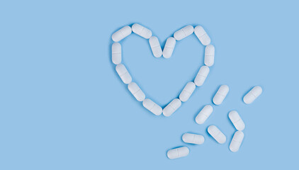 White pills in shape of heart on the blue background. Medicine concept. Flatlay. Top view. Place for text. Close-up.