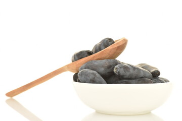 Several dark blue organic ripe honeysuckle berries in a white bowl with a wooden spoon, close-up,...