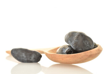 Several dark blue organic ripe honeysuckle berries with a wooden spoon, close-up, isolated on white.