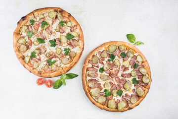 Two pizzas with different fillings with Caesar sauce, pork, bacon, pickles, sausage, tomatoes and Mozzarella cheese on a light background.