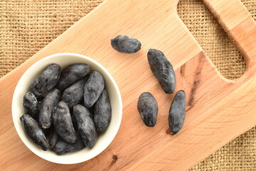 Several dark blue organic ripe honeysuckle berries in a white saucer on a wood board, close-up, top view.