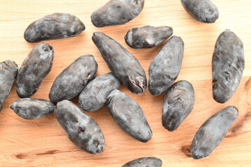 Several dark blue organic ripe honeysuckle berries on a wood board, close-up, top view.