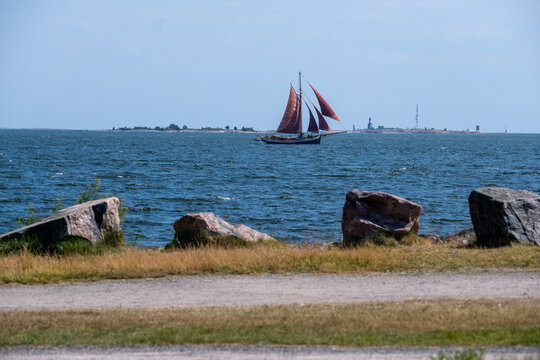 A view towards the sea from the shore. A traditional sailboat crossing the horizon at the distance.