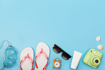 Top view photo of sunscreen diving mask, sneaker, alarm clock, seashells, camera from above, on isolated blue background with copyspace