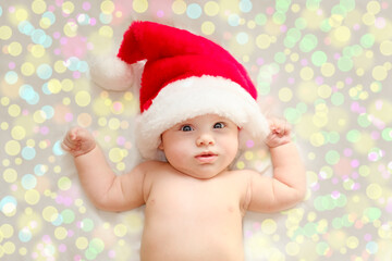 Beautiful little child is celebrating Christmas. New Year's holidays. A child in a Christmas costume. Childhood and people concept - happy Newborn baby in Santa hat over holidays lights background