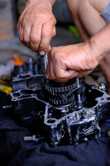 A motorcycle mechanic is working on the engine gear.