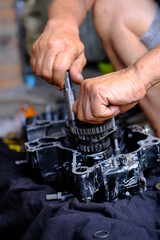 A motorcycle mechanic is working on the engine gear.	