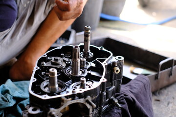 A motorcycle mechanic is working on the engine gear.