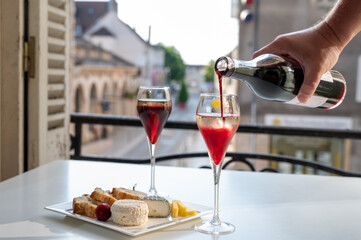 Drinking of Kir Royal,  French aperitif cocktail made  from creme de cassis topped with champagne, typically served in flute glass, with view on old French village